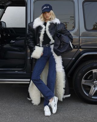 Woman wearing a long fur-lined coat, jeans, and sneakers.