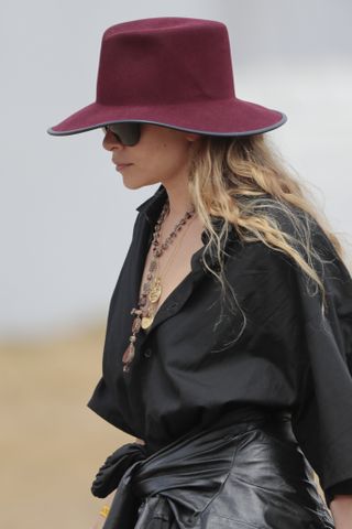 Ashley Olsen wearing a black top with layered necklaces and a red wide-brimmed hat.