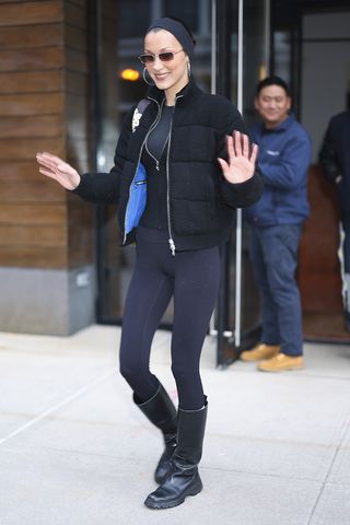 Bella Hadid wearing a puffer, leggings, and boots in NYC.