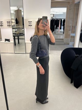 Eliza Huber wearing an all-gray outfit at the Alaia store in Paris trying on a navy blue Le Teckel shoulder bag.