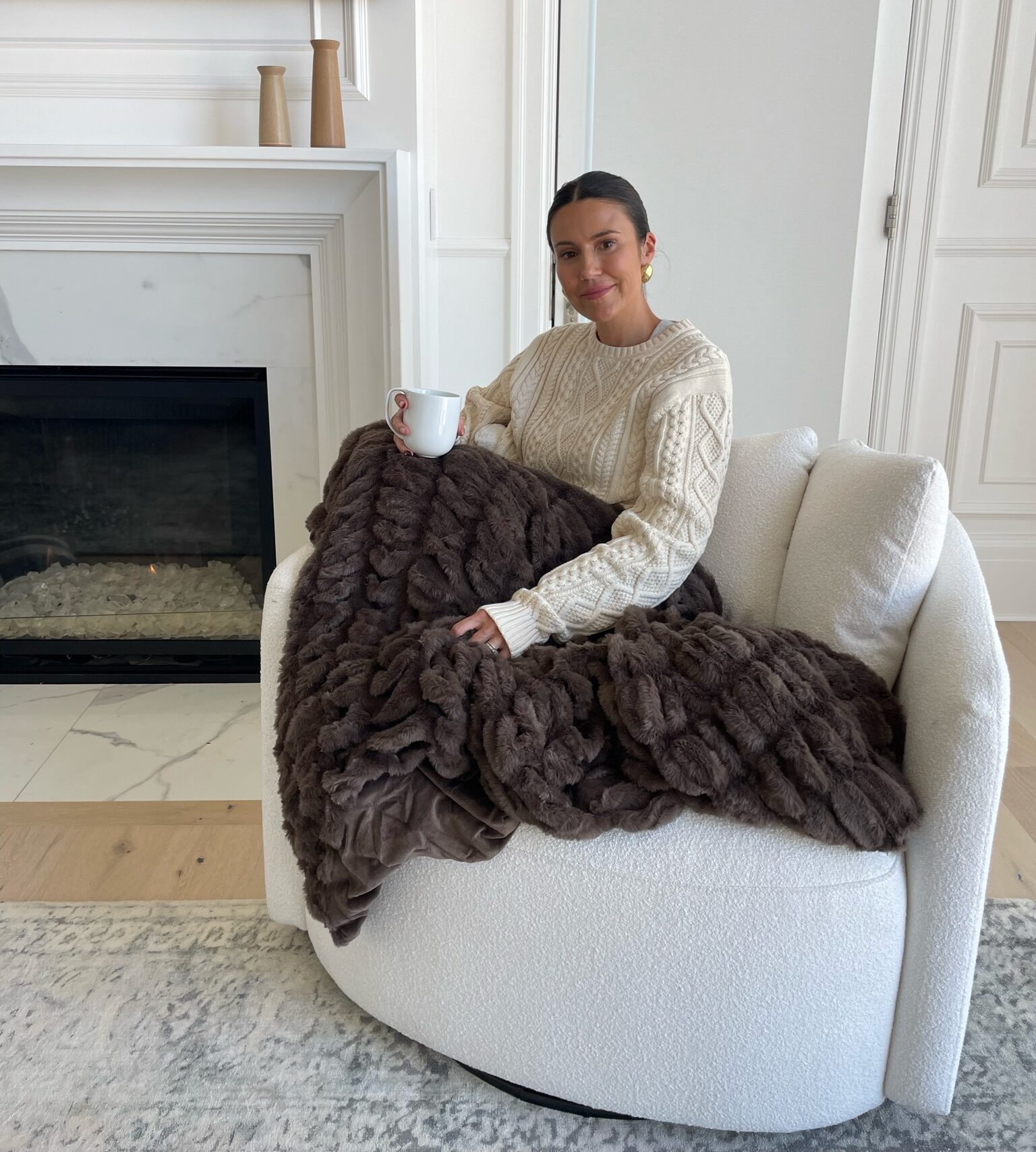 Christine Andrew with a cozy soft brown blanket on her white swivel accent chair at home.