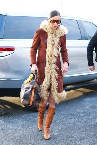 Bella Hadid wears a brown penny lane coat, tan knee-high boots and a louis vuitton duffle bag.