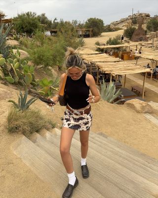 Sofia Coelho in a a black tank top, cow print skirt, and loafers.