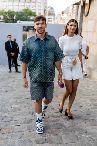 Couple Pierre Gasly wears shirt and shorts with logo print and Francisca Gomes wears white skirt, top outside Louis Vuitton during the Menswear Spring/Summer 2024 as part of Paris Fashion Week on June 20, 2023 in Paris, France.