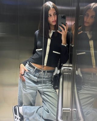 French influencer and model Salome Mory poses for an elevator selfie with a long bob, contrast trim cardigan, a skinny black belt, baggy straight-leg jeans, and black Onitsuka Tiger Mexico 66 sneakers.