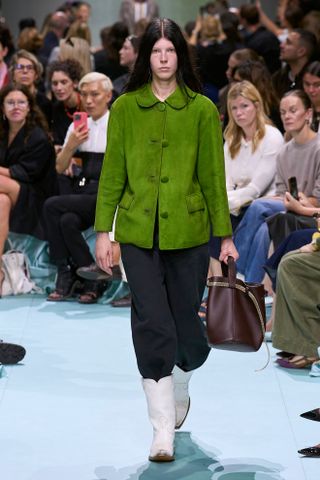 Woman in emerald green jacket on the SS25 Prada runway.