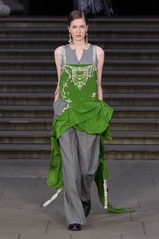 Woman in emerald green dress over gray pants on the spring 2025 Erdem runway.