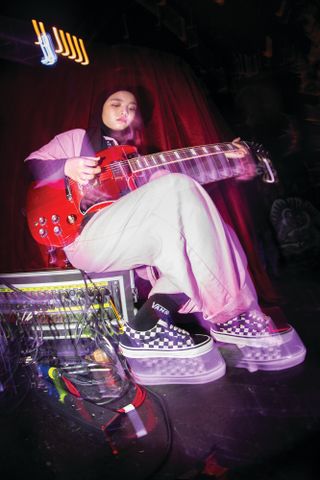 a woman plays guitar and wears Vans sneakers