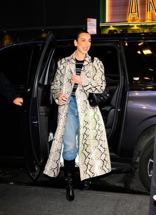 Dua Lipa wearing snake-print coat, jeans, and black boots