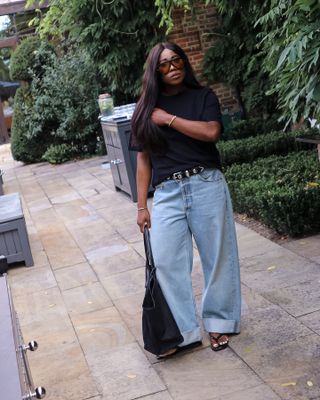 Woman wears black t-shirt, blue jeans and studded belt