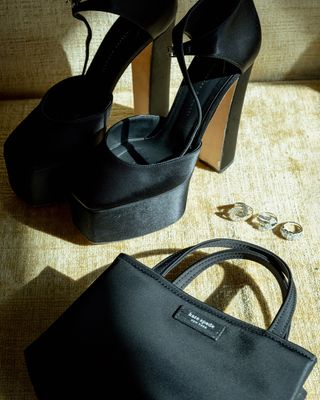 A still life portrait of Maisy Stella's accessories for the Critics Choice Awards, featuring black satin Giuseppe Zanotti heels, a black top-handle Kate Spade bag, and Effy Jewelry rings.