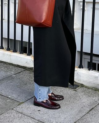 British influencer Anna Newton wearing a long black coat, straight-leg jeans, and burgundy ruched loafers