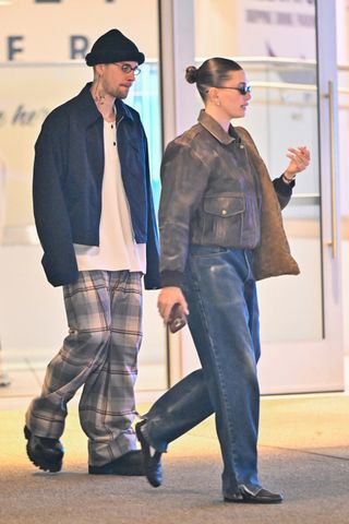 Hailey Bieber wears a brown distressed leather jacket, bottega veneta suede bag, blue jeans, white socks, and black loafers.