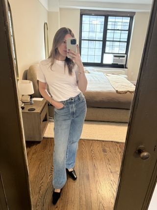 Nikki wears a white t-shirt, jeans, and black heels.