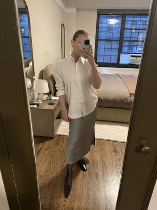 Nikki wears a white button-down shirt, silk skirt, sheer tights, and black heels.