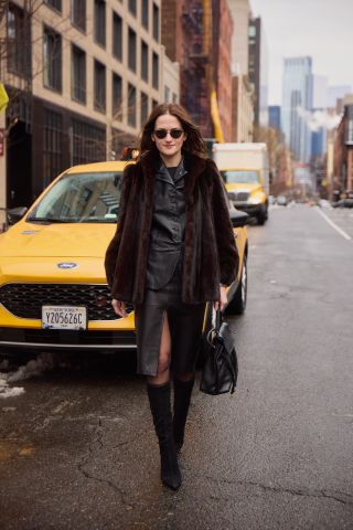 Eliza Huber wearing a brown fur coat, black leather jacket, black pencil skirt, black tights, black suede boots, and black sunglasses while carrying a black Bottega Veneta Ciao Ciao bag outside of the Ulla Johnson show in Soho.