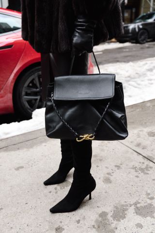 Eliza Huber wearing a brown fur coat, black leather jacket, black pencil skirt, black tights, black suede boots, and black sunglasses while carrying a black Bottega Veneta Ciao Ciao bag outside of the Ulla Johnson show in Soho.