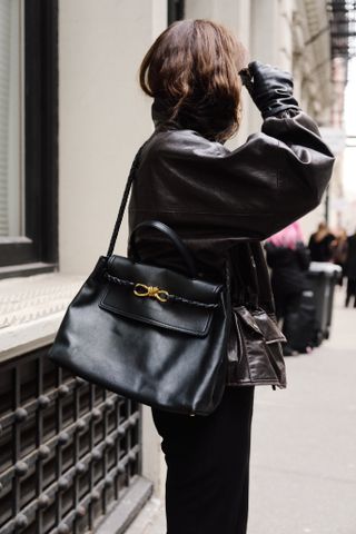 Eliza Huber wearing a brown leather jacket, black trousers, white loafers, and black sunglasses, while carrying a black Bottega Veneta Ciao Ciao bag outside of the Kallmeyer show in Tribeca.