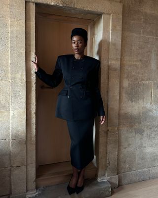 @nlmarilyn wearing a black outfit, including a pillbox hat, sculpted blazer, pencil skirt, and pumps.