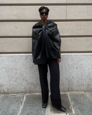 @thevisuelofgrace wearing a black Marina Moscone cape with black trousers and black heels.