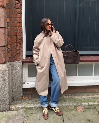 woman wearing cuffed denim outfit with trench coat and suede sneakers