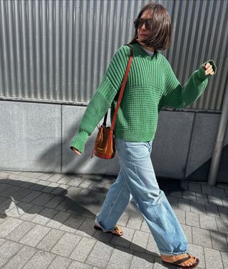 woman wearing cuffed denim outfit with green sweater and flip flops