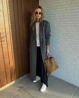 Anouk wears a gray wool coat, white shirt, black pants, and white sneakers.