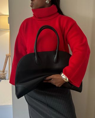 Woman in red jumper, pinstripe skirt carries black handbag