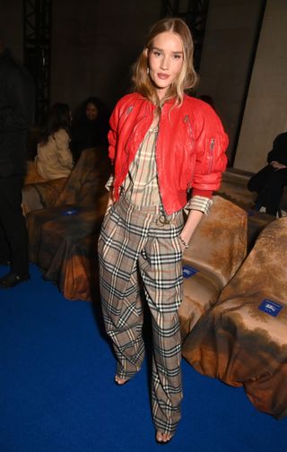 Rosie Huntington-Whiteley front row at the Burberry fall/winter 2025 show in London wearing checkered trousers, a checkered shirt, and red leather bomber jacket