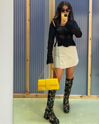 @miraalmomani wears a bright yellow Jacquemus bag with statement boots and a miniskirt