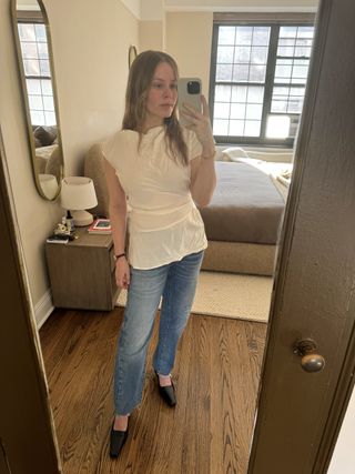 Nikki wears a white blouse, jeans, and black pumps