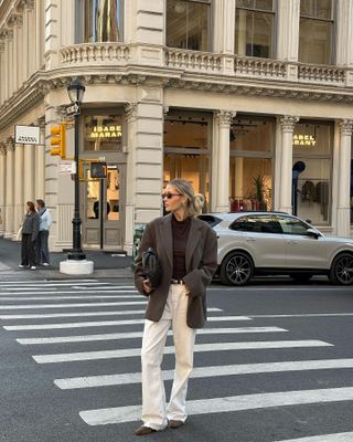 Fashion influencer @fredrika_ekerot in New York wearing an anti-trend outfit styled with belted cream jeans, an oversize blazer, a brown top, and brown suede flats.