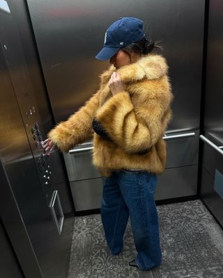 Fashion influencer @mimixn in New York wearing an anti-trend outfit styled with a faux fur jacket, a New York Yankees cap, and relaxed blue jeans.