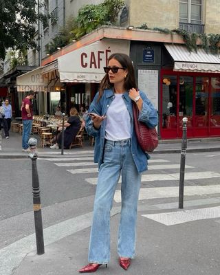 Fashion influencer @leasy_inparis in Paris wearing an anti-trend outfit styled with a denim shirt, jeans, a white T-shirt, a burgundy bag, and burgundy pumps.