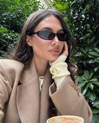 Fashion influencer @borislavasekova sitting outside at a cafe wearing a chic spring outfit for 2025.