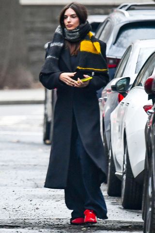 Emily Ratajkowski wearing a black coat, black pants, and red sneakers