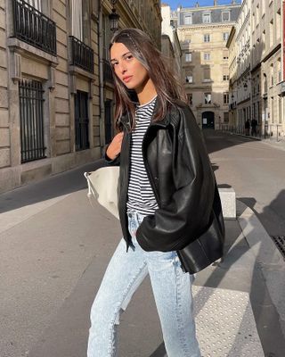 French influencer and model Salome Mory walking on the streets of Paris wearing a black leather jacket, stripes tee, and light-wash skinny jeans