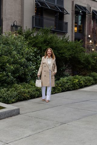 A Nordstrom stylist wearing a long tan trench coat and white pants.