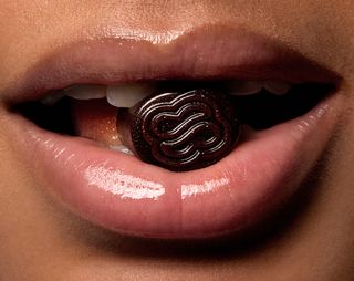 Woman holding one of Sakara's Metabolism Bite gummy supplements between her teeth.