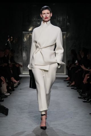 A model wearing a white tailored blazer and trousers walking in Haider Ackermann's first Tom Ford runway show during Paris Fashion Week.