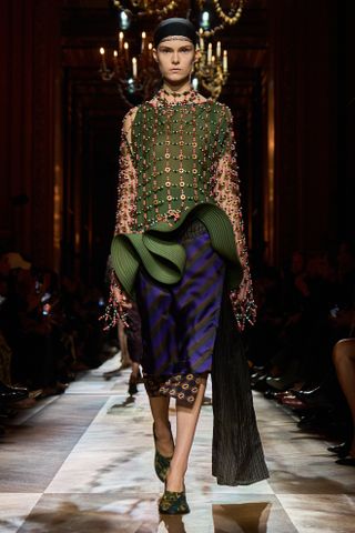 A model wearing a beaded top with a sculptural skirt and round-toe heels while walking at the F/W 25 Dries Van Noten show during Paris Fashion Week.