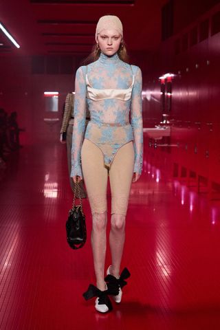 A model walking in the F/W 25 Valentino show during Paris Fashion Week wearing a lace bodysuit with lace pedal pushers and a satin bralette.