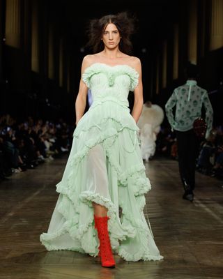 A model wearing a soft jade strapless gown with red boots at the Alexander McQueen F/W 25 show during Paris Fashion Week.