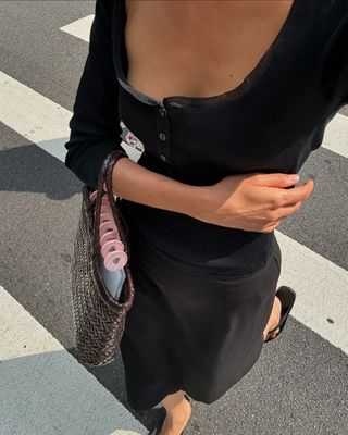 @shayinjune walking with a black fitted top, black midi skirt, and brown woven bag