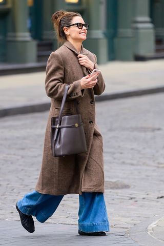 Katie Holmes wearing a brown coat, wide-leg jeans, and black ruched ballet flats in NYC