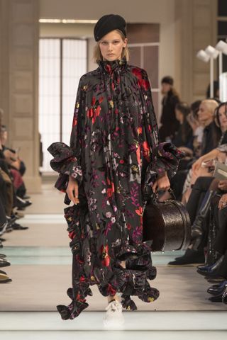 A model wearing a black hat and velvet-printed floral caftan at the Louis Vuitton F/W 25 show.