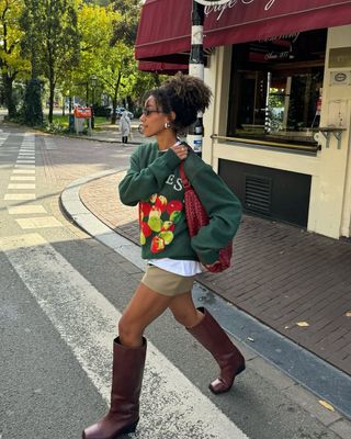 Woman wearing crewneck and tan miniskirt with tall brown boots.