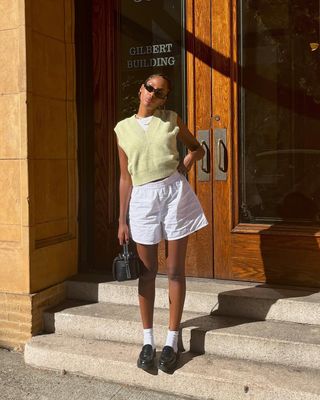 woman wearing yellow vest sweater, white linen shorts, and loafers