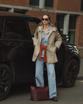 Woman wearing a short trench coat with light wash jeans.