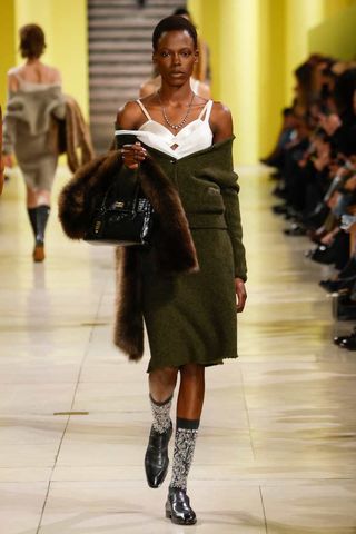 A satin bra, green cashmere sweater and skirt set, and fur coat from the F/W 25 Miu Miu runway collection.